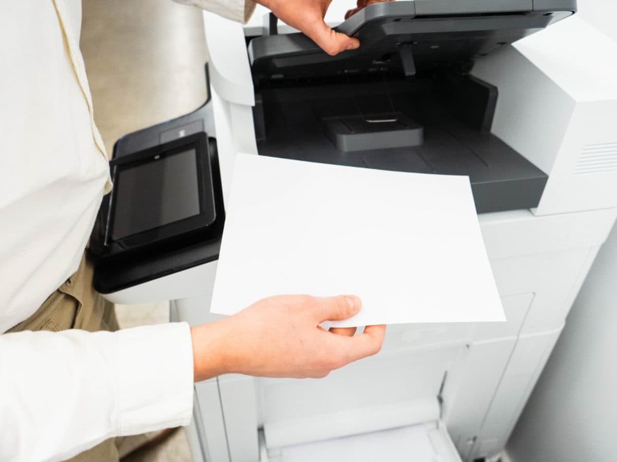 Hands feeding paper into a high-volume office copier during a document production run.